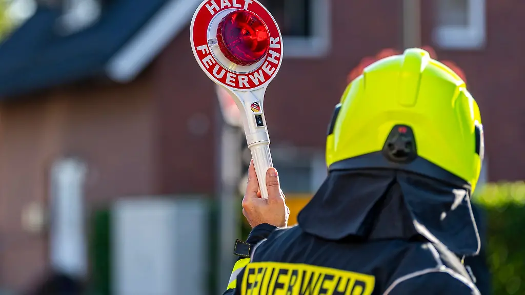 Ein-Feuerwehrmann-haelt-eine-Kelle-in-die-Hoehe-um-den-Verkehr-zu-stoppen