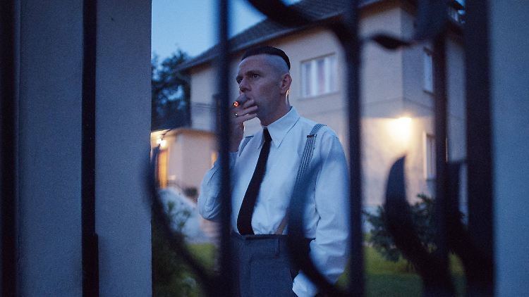 Rudolf Höß, in "The Zone of Interest" gespielt von Christian Friebel, steht am Tor seines Gartens in Auschwitz und raucht.