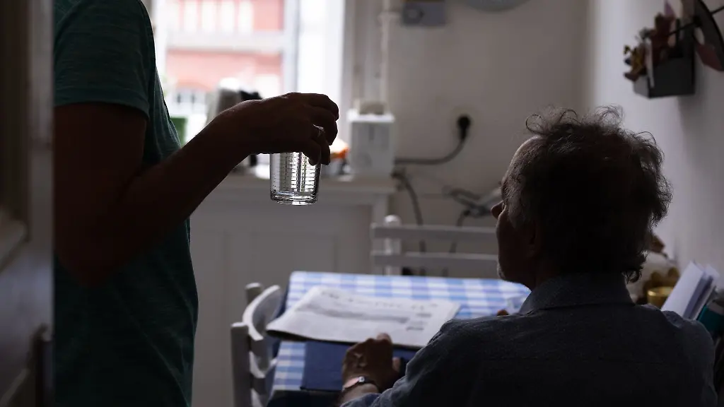 Eine-Pflegerin-reicht-ihrem-Patienten-bei-einem-Hausbesuch-ein-Glas-Wasser