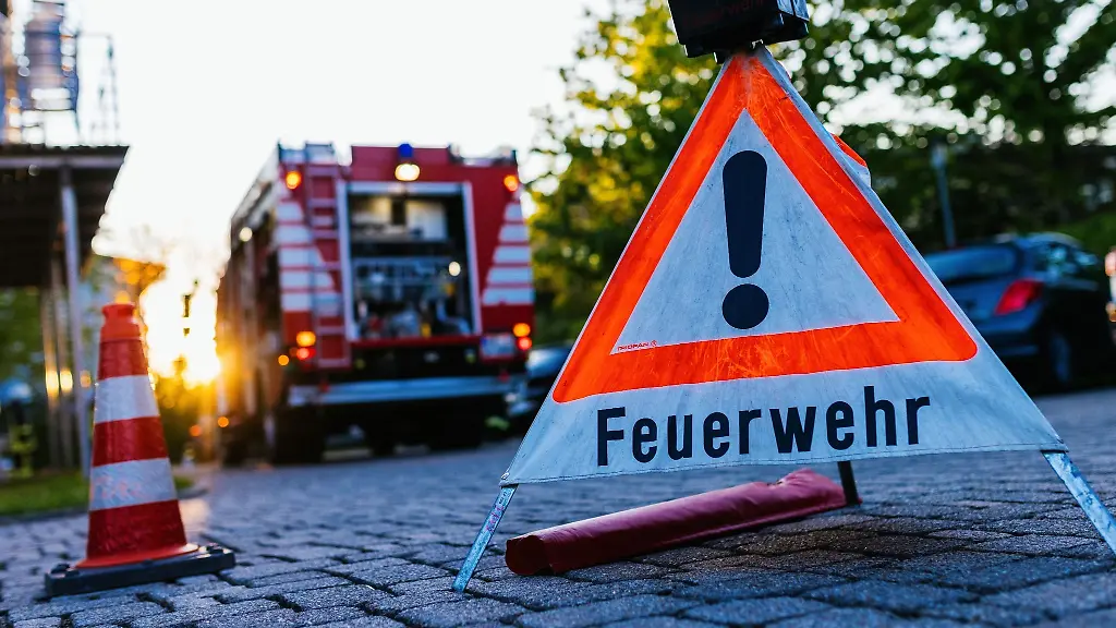 Ein-Warndreieick-mit-der-Aufschrift-Feuerwehr-steht-auf-dem-Hof-eines-Feuerwehrgeraetehauses