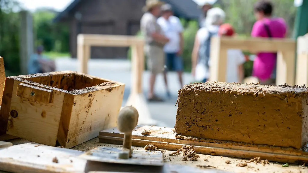 Ein-frisch-gestampfter-Lehmziegel-und-Werkzeug-liegt-auf-einem-Tisch