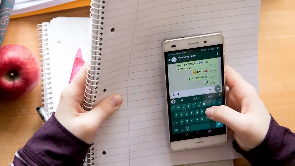 Eine-Schuelerin-sitzt-mit-ihrem-Handy-und-ihren-Schulsachen-an-einem-Schreibtisch