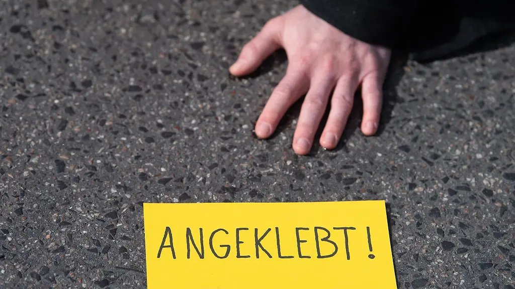Ein-Demonstrant-ist-bei-einem-Protest-der-Gruppe-Letzte-Generation-auf-einer-Strasse-festgeklebt