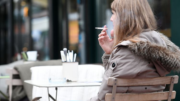 Eine Frau raucht im Außenbereich eines Cafés eine Zigarette.