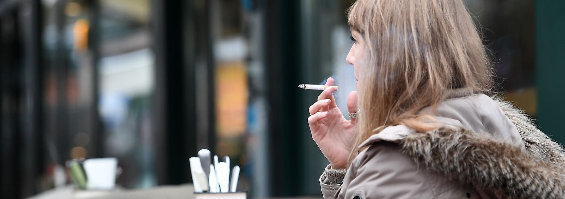Eine Frau raucht im Außenbereich eines Cafés eine Zigarette.