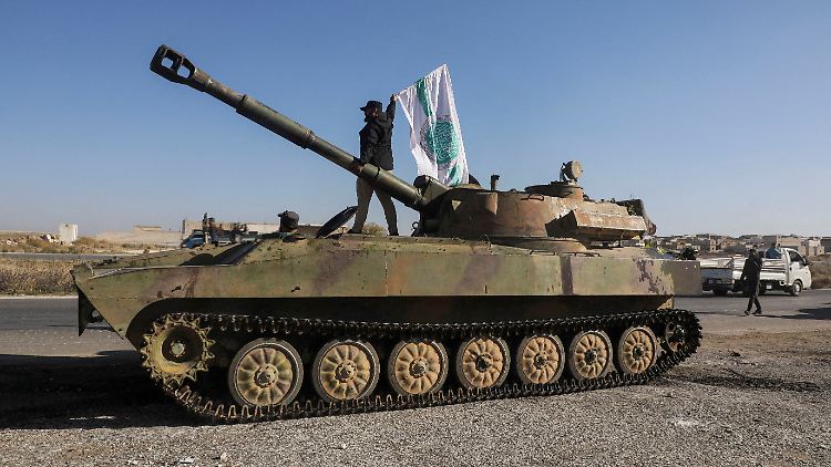Ein oppositioneller Kämpfer steht auf einem Militärfahrzeug und hält eine Flagge der islamistischen Gruppe Hayat Tahrir al-Sham. 