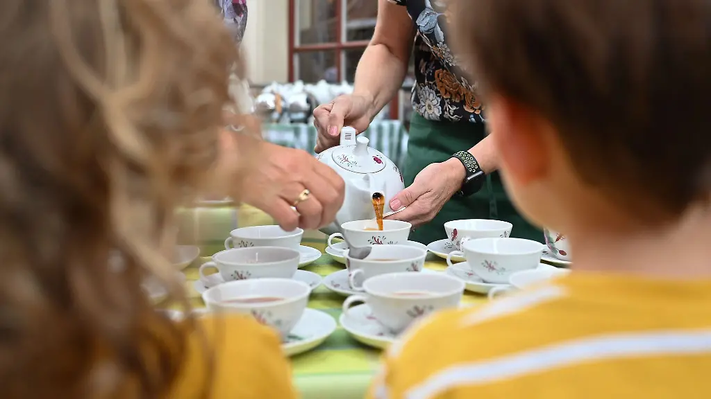 Zwei-Mitarbeiter-des-Teemuseums-schenken-unter-den-Augen-zweier-junger-Gaesten-Tee-nach-Ostfriesischer-Art-ein