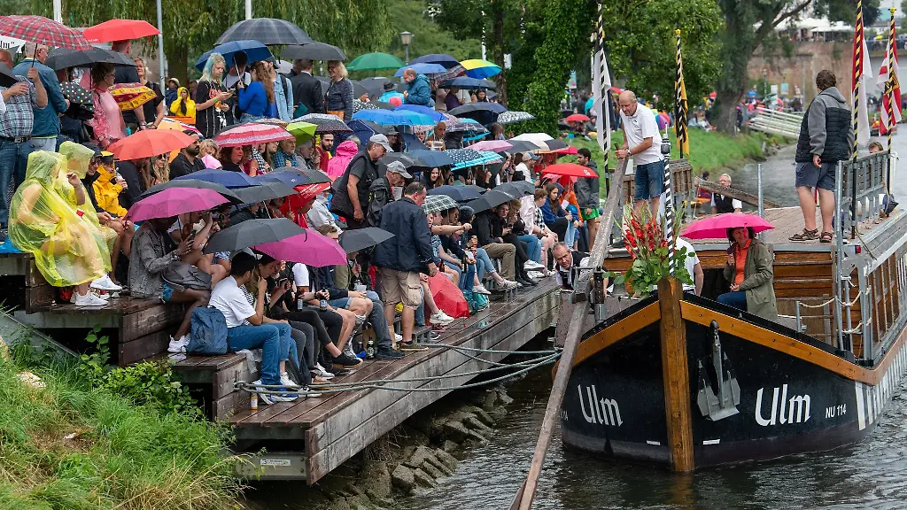 Unter-Regenschirmen-sitzen-Zuschauer-auf-einer-Tribuene-am-Ufer-der-Donau