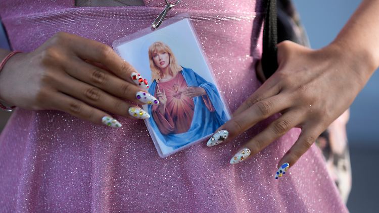 Ein Fan hält eine gebetsähnliche Karte, die Taylor Swift in der Art des Heiligsten Herz Jesu simuliert.