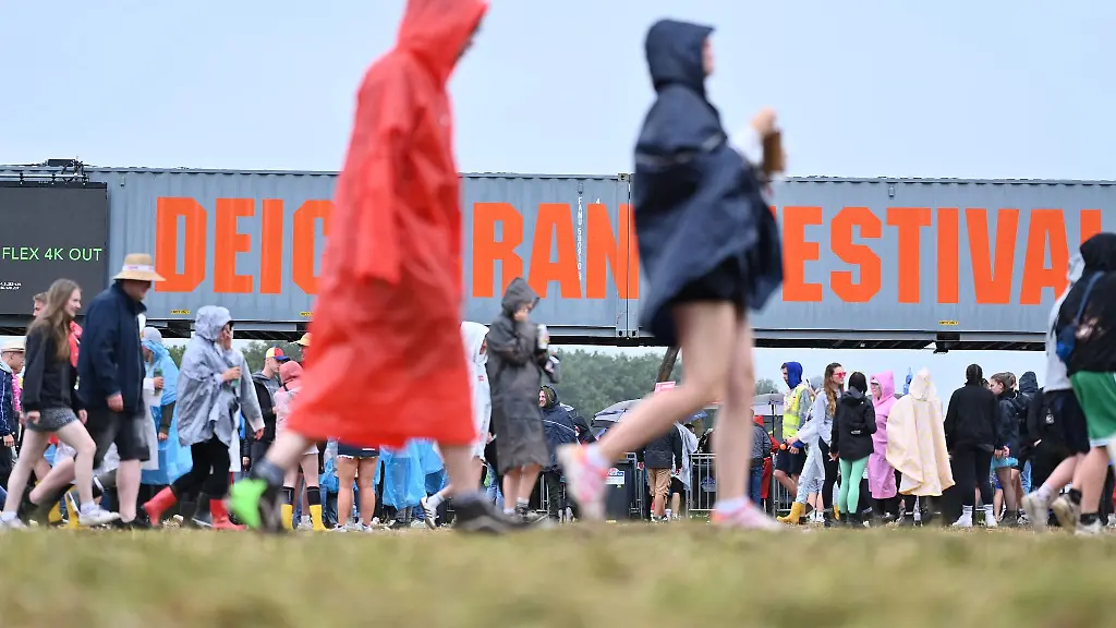 Festival-Besucher-ziehen-mit-Regen-Ponchos-uebers-Gelaende