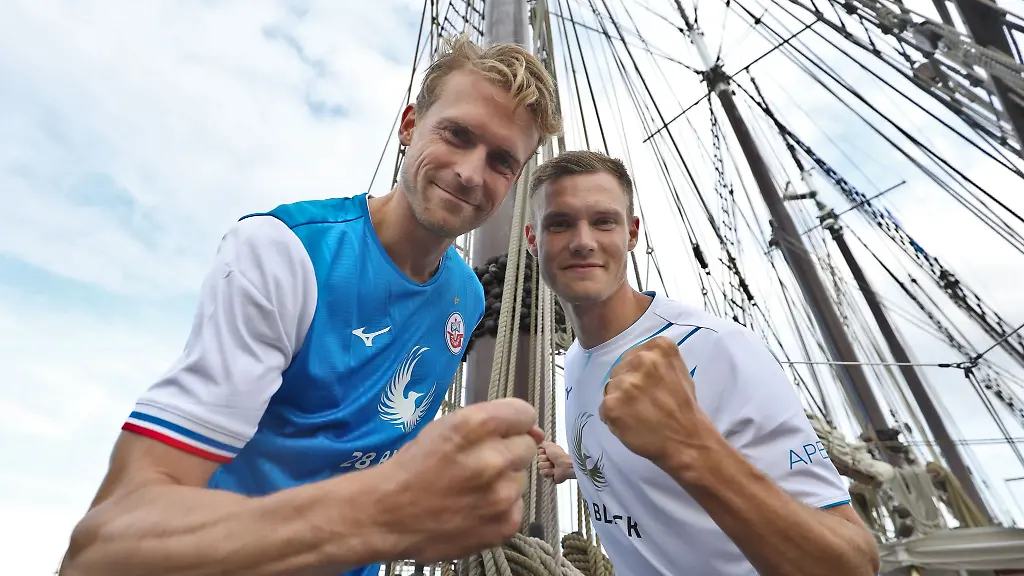 Oliver-Huesing-l-und-Svante-Ingelsson-praesentieren-die-neuen-Trikots-zum-Saisonauftakt-des-Fussball-Zweitligisten-FC-Hansa-Rostock-auf-dem-Deck-des-Segelschiffes-Santa-Barbara-Anna-im-Rostocker-Stadthafen