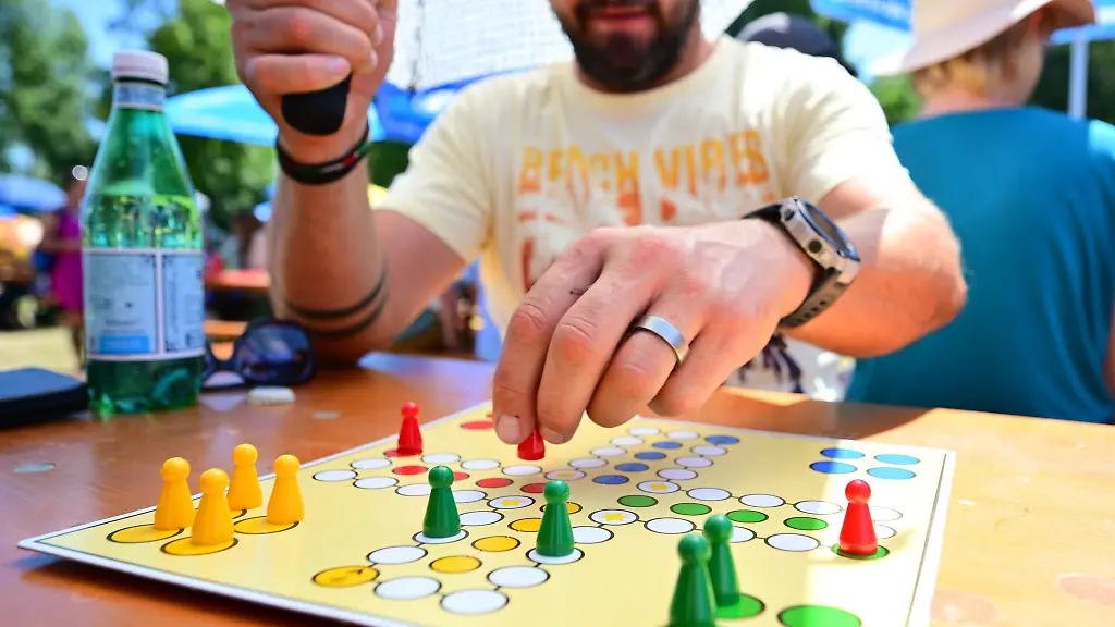 Ein-Spieler-versucht-sich-beim-Mensch-aergere-dich-nicht-mit-einem-Schirm-vor-der-Sonne-zu-schuetzen