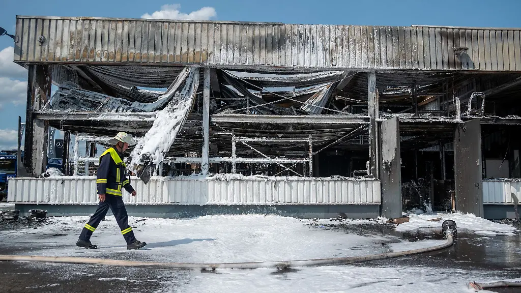 Ein-Feuerwehrmann-geht-nach-Loescharbeiten-an-einem-verbrannten-Autohaus-vorbei