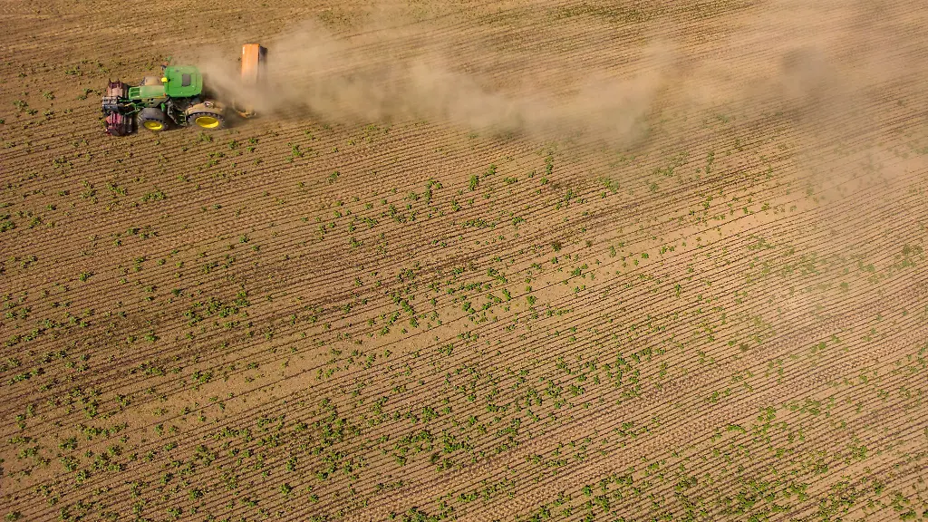 Ein-Traktor-faehrt-mit-einem-Haecksler-ueber-ein-trockenes-sandiges-Feld