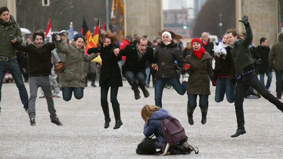 Eine Gruppe jugendlicher Touristen springt für ein Foto am Brandenburger Tor in die Luft: trotz Kältegraden und ungemütlichem Wetter ist Berlin eine Reise wert.