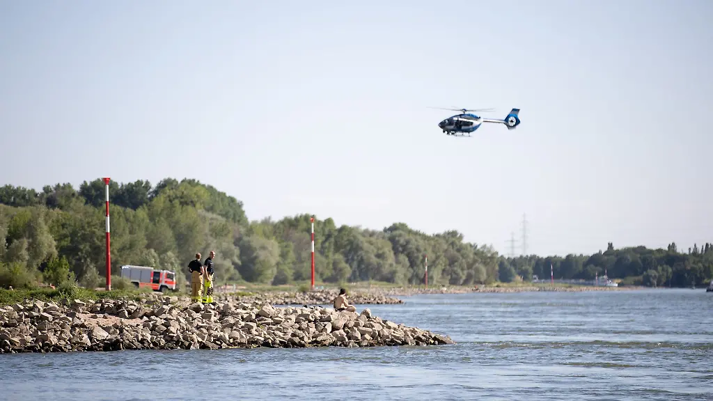 Aus-einem-Hubschrauber-und-vom-Ufer-aus-suchen-Einsatzkraefte-nach-dem-Schwimmer-der-von-einem-Sog-erfasst-und-mitgerissen-wurde