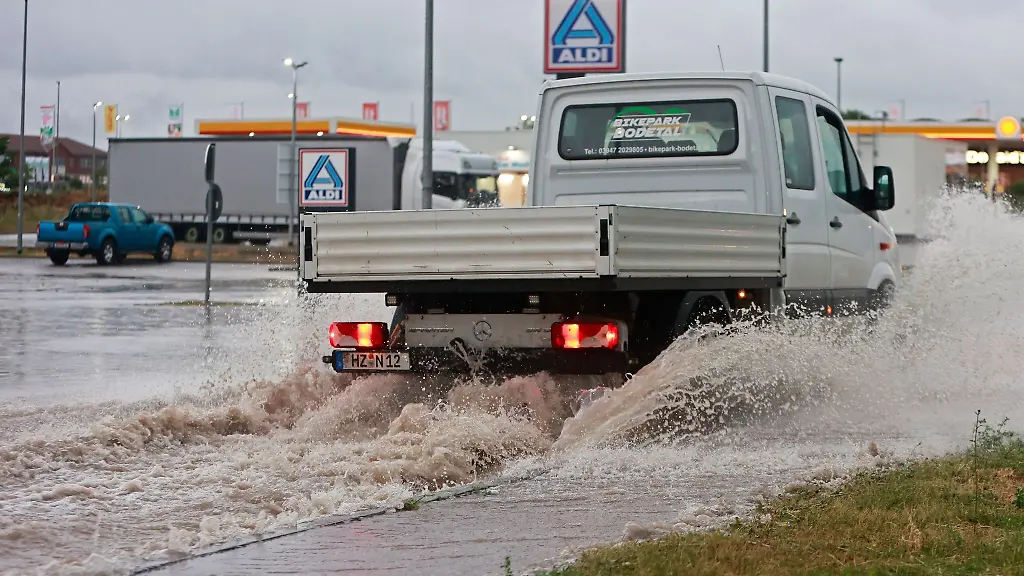 Ein-Kleintransporter-faehrt-nach-einem-Unwetter-mit-Starkregen-ueber-eine-ueberflutete-Strasse-in-einem-Gewerbegebiet