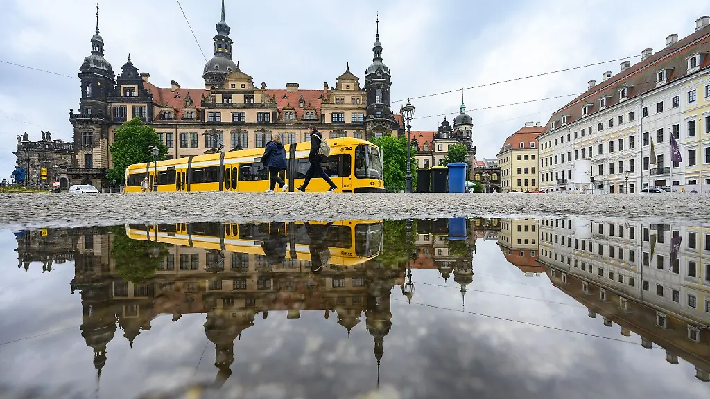 Eine-Strassenbahn-der-Dresdner-Verkehrsbetriebe-DVB-faehrt-in-der-Altstadt-vor-dem-Residenzschloss-entlang-und-spiegelt-sich-in-einer-Pfuetze