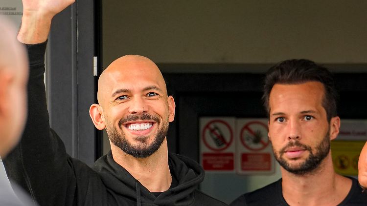 Andrew Tate winkt neben seinem Bruder Tristan auf einer Polizeistation in Rumänien.