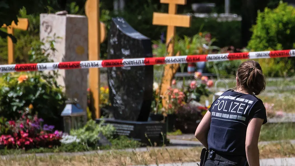 Eine-Polizistin-geht-ueber-den-abgesperrten-Teil-an-einem-Tatort-auf-einem-Friedhof