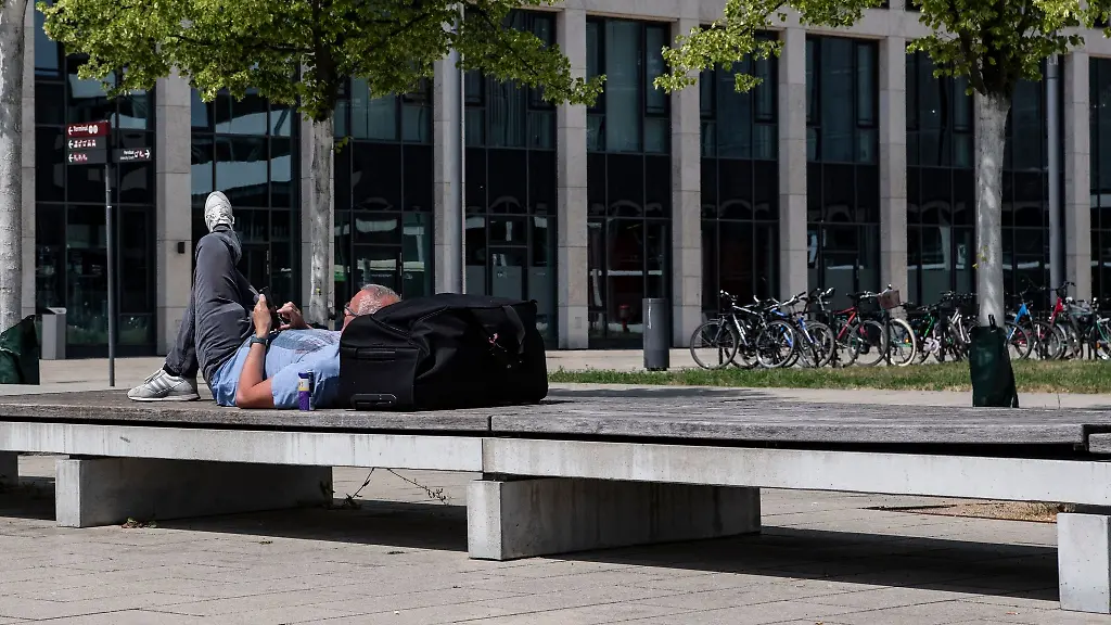 Ein-Reisender-liegt-am-Flughafen-in-der-Sonne-und-schaut-auf-sein-Handy