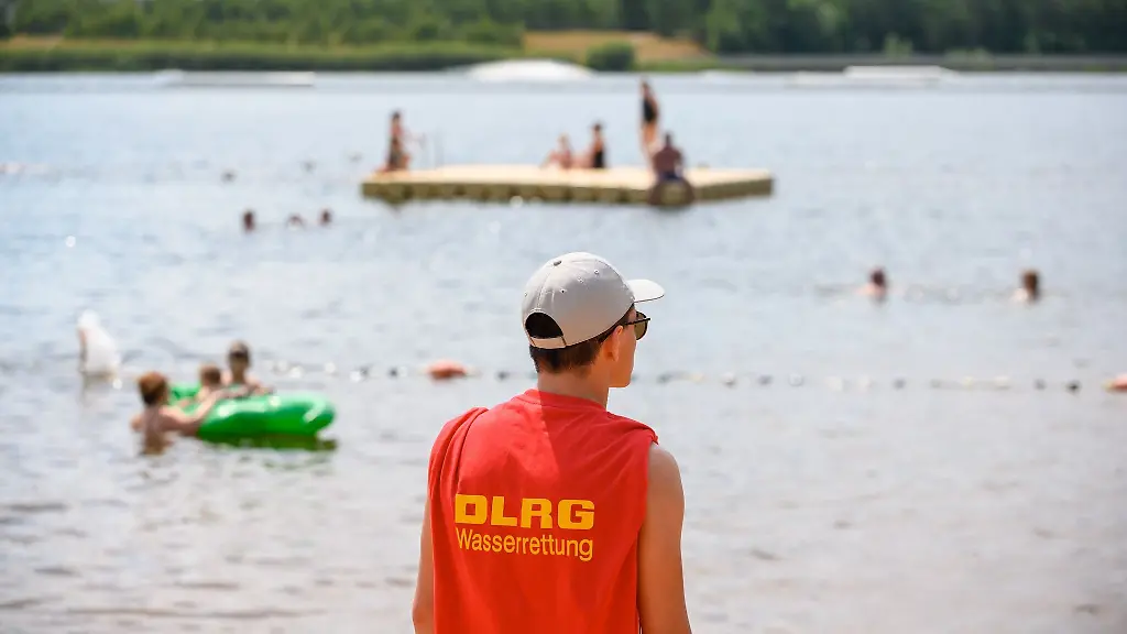 Ein-Mitglied-der-Deutschen-Lebens-Rettungs-Gesellschaft-DLRG-steht-in-einem-Strandbad-am-Ufer