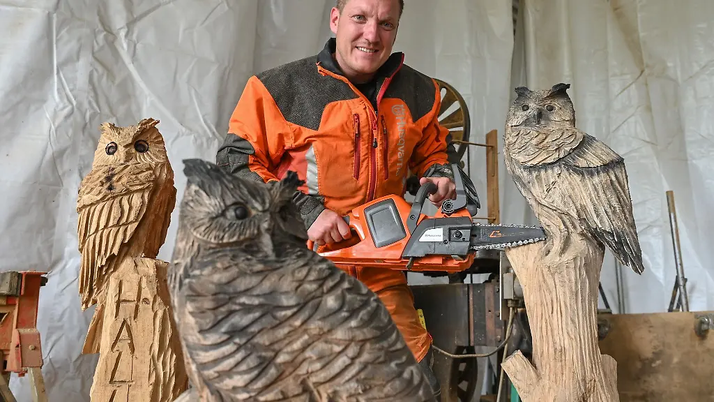 Der-Kettensaegen-Kuenstler-Christian-Muecke-steht-in-seiner-Werkstatt-vor-Uhu-Figuren-aus-Holz
