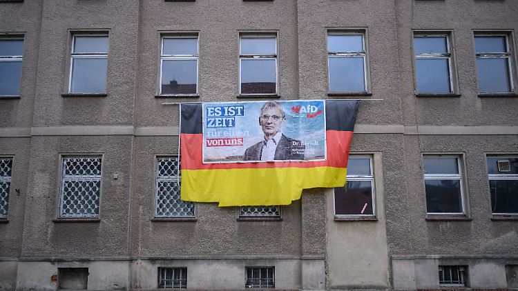 Ein älteres Wahlplakat von Hans-Christoph Berndt, Vorsitzender der Brandenburger AfD-Fraktion, hängt auf einer Deutschlandflagge an einer tristen Hausfassade.