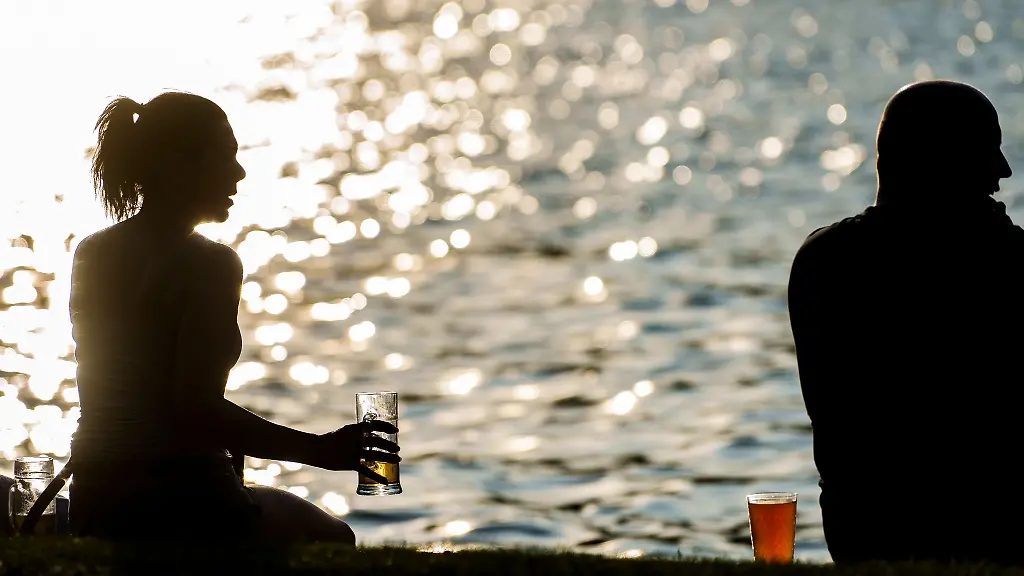 Eine-Frau-sitzt-in-der-untergehenden-Abendsonne-am-Mainufer-und-nimmt-ein-Getraenk-zu-sich