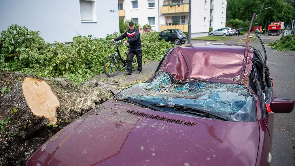 Ein-Mann-geht-nach-einem-Sturm-an-einem-zerstoerten-Auto-vorbei