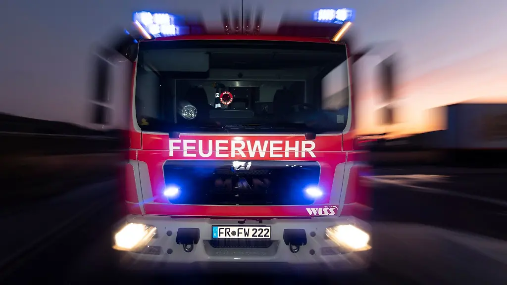 Ein-Feuerwehrfahrzeug-steht-mit-eingeschaltetem-Blaulicht-im-Sonnenuntergang-auf-einer-Strasse