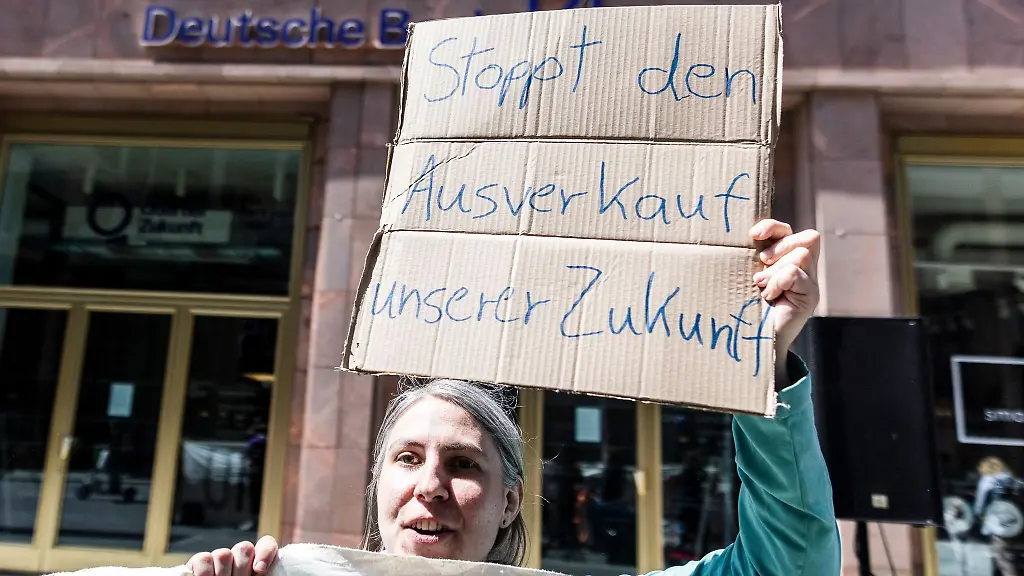 Demonstrantin-mit-Schild-Stoppt-den-Ausverkauf-unserer-Zukunft-vor-einer-Deutschen-Bank-Filiale
