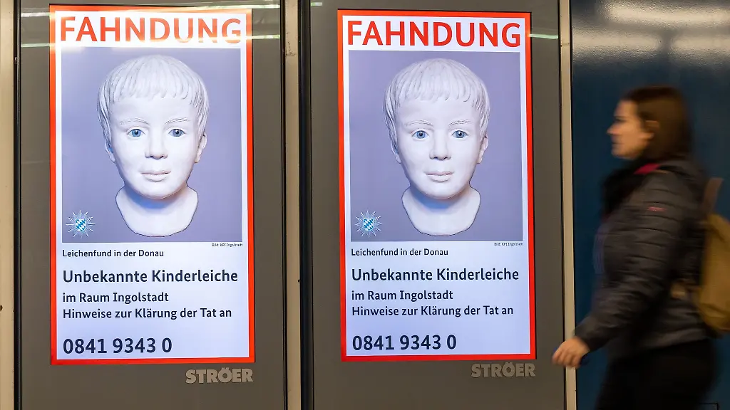 Eine-Frau-geht-an-einem-digitalen-Fahndungsplakat-vorbei-Mit-der-Veroeffentlichung-wollten-die-Ermittler-den-Fall-eines-toten-Buben-aus-der-Donau-klaeren-Knapp-ein-Jahr-nach-dem-Fund-des-Leichnams-gibt-es-weiter-keine-Hinweise-auf-den-Taeter-Auch-die-Identitaet-des-Kindes-ist-immer-noch-unklar