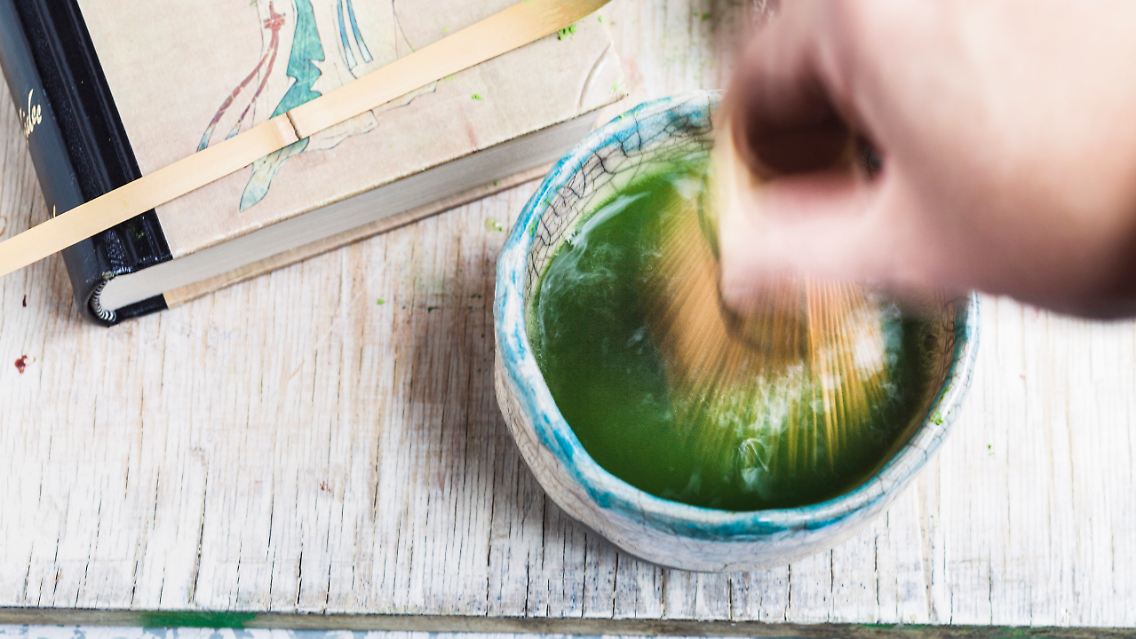 Nur eine kleine Löffelspitze Matcha wird mit aufgeschäumter Milch oder traditionell mit heißem Wasser in einer Keramikschale angerührt.