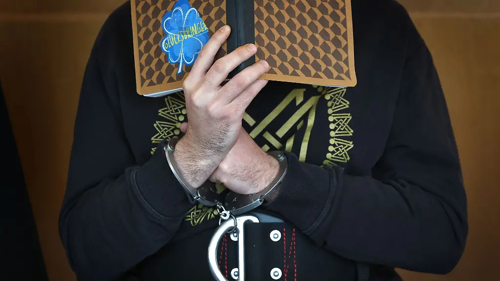 Ein-junger-Mann-sitzt-in-einem-Gerichtssaal-im-Landgericht-auf-der-Anklagebank-und-verbirgt-sein-Gesicht