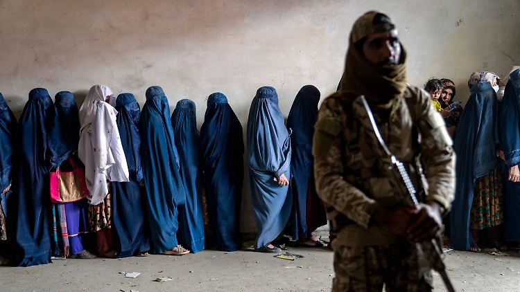 Ein Taliban bewacht eine Schlange von Frauen, die bei einer Essensausgabe anstehen.