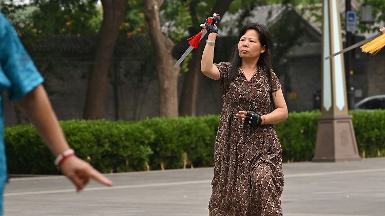 Frau Wei führt auf einem Platz in Peking mit einem Schwert eine Tai-Chi-Übung aus.