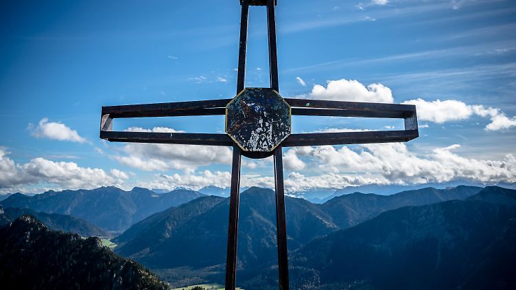 Das Gipfelkreuz des Teufelsstättkopf ist vor dem Panorama der Ammergauer Alpen zu sehen.