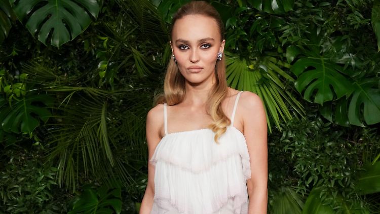 Schauspielerin Lily-Rose Depp schaut in typischer roter Teppich-Pose mit kühler Miene in die Kamera.