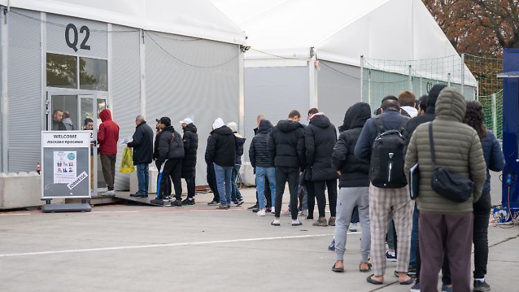 Geflüchtete stehen vor einer Halle am ehemaligen Berliner Flughafen Tegel an. 