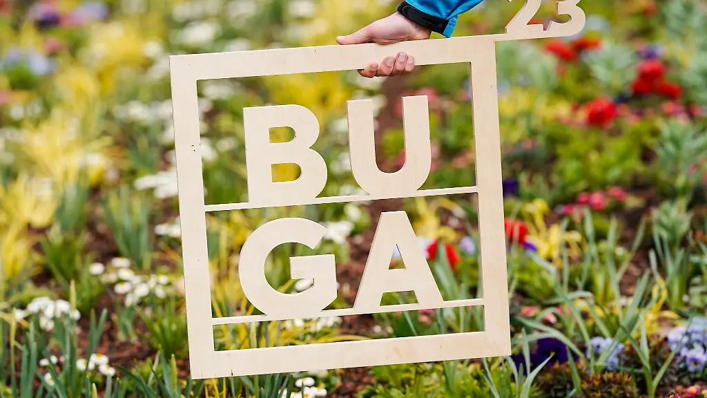 Ein-Holzrahmen-mit-der-Aufschrift-BUGA-23-wird-in-Mannheim-vor-ein-Blumenbeet-gehalten