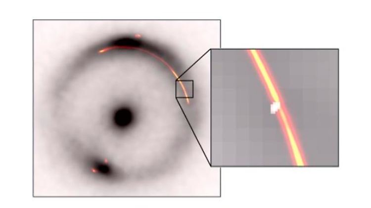 Der schwarze Ring und der zentrale Punkt zeigen das Infrarotbild einer entfernten Galaxie, das durch eine Gravitationslinse verzerrt wurde. Die orangenen und roten Bereiche zeigen Radiowellen desselben Objekts. Die Einblendung zeigt eine Verengung, die durch eine andere, viel kleinere, dunkle Gravitationslinse (weißer Fleck) verursacht wurde.