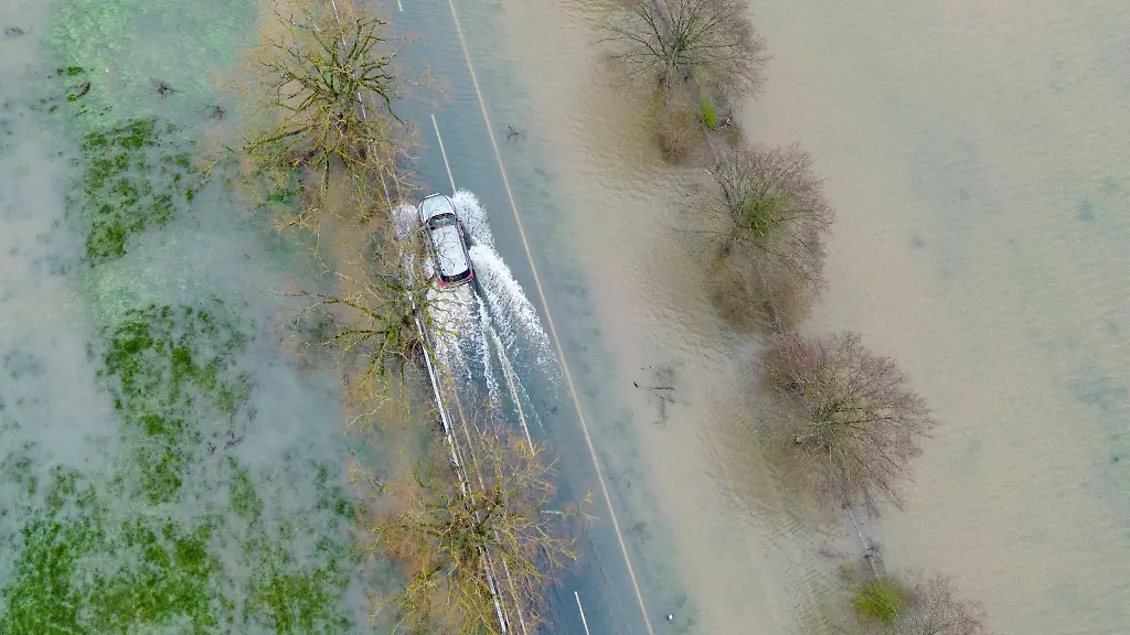 Ein-Auto-faehrt-ueber-eine-vom-Hochwasser-ueberflutete-Landstrasse-in-Mittelhessen