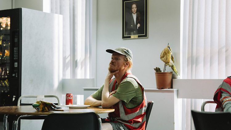Teddy im Pausenraum, wo ein Foto von Konzernboss Michelle an der Wand hängt.