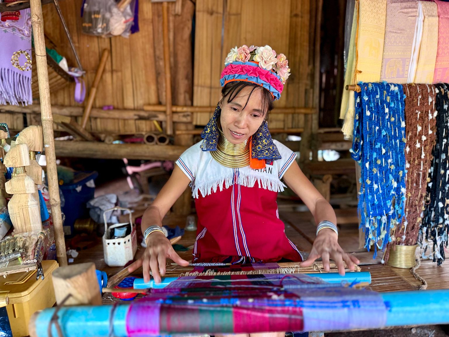 Am Rand der Berge nördlich von Chiang Rai sitzen Frauen vor ihren Hütten und weben flink bunte Schals. An einer Bambusstange wehen die fertigen Handarbeiten im Wind. 