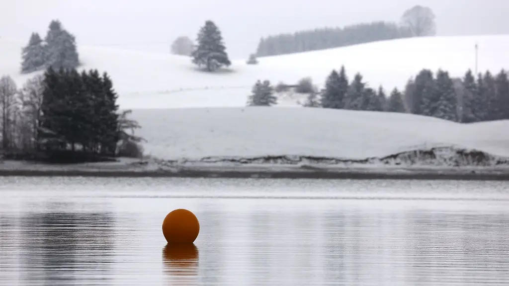 Eine-Boje-treibt-auf-dem-in-schneebedeckter-Landschaft-liegenden-Forggensee