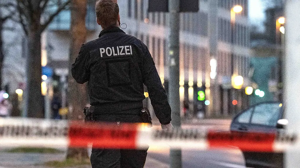 Ein-Polizist-geht-hinter-einem-Absperrband-entlang