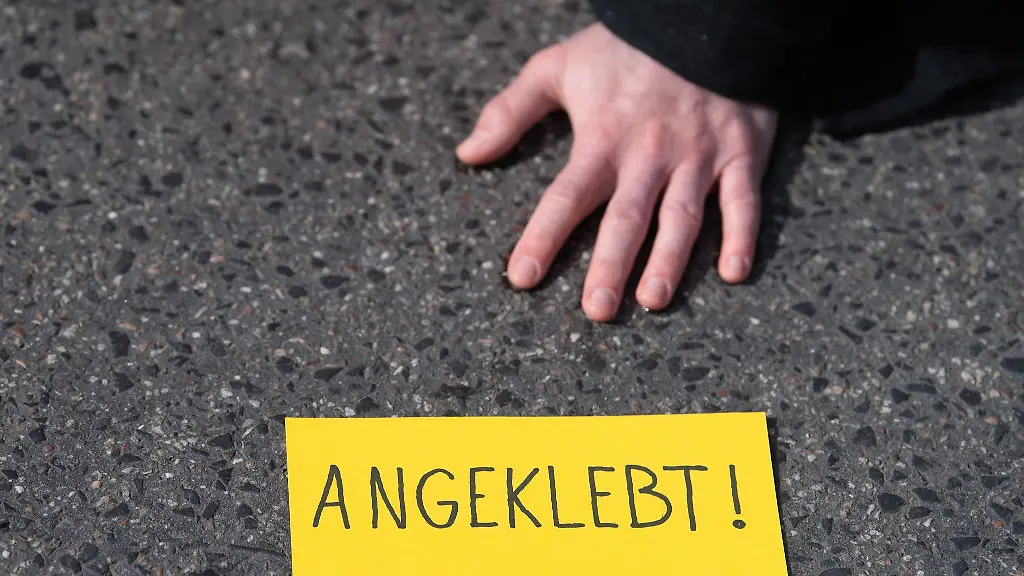 Ein-Demonstrant-ist-bei-einem-Protest-der-Gruppe-Letzte-Generation-auf-einer-Strasse-festgeklebt