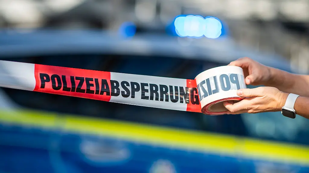 Ein-Absperrband-wird-vor-einem-Polizeiwagen-ausgerollt