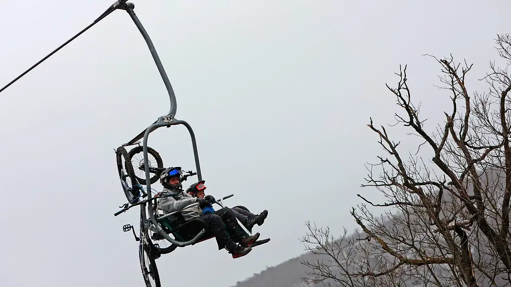 Zwei-Maenner-sitzen-mit-ihren-Mountainbikes-in-einem-Sessellift